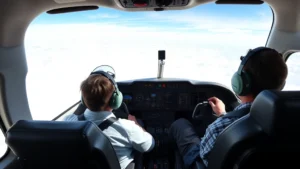Modern aircraft cockpit with pilot and copilot during daytime flight operations, showing instrument panels and windows with clouds below