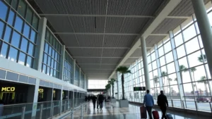 Modern Orlando International Airport MCO terminal interior with tall ceilings, contemporary architecture, palm trees visible through windows, bright natural lighting, travelers walking with luggage