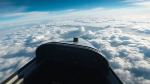 Aerial view of commercial aircraft cockpit during daytime flight with clouds below, pilots visible through windscreen, realistic photography