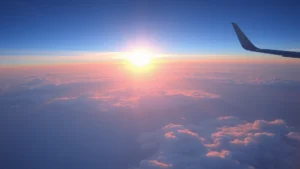 Pacific Ocean sunrise view from aircraft window during transpacific flight, fluffy clouds below, golden light breaking through