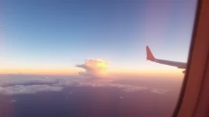 Sunset view from airplane window over Pacific Ocean with golden light reflecting on clouds during westbound flight to Asia