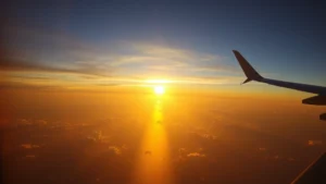 Aerial view of Atlantic Ocean at sunrise with aircraft wing visible, golden light reflecting on water, dramatic cloudscape below, photorealistic travel photography