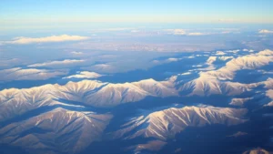 Rocky Mountains landscape with Denver skyline visible in distance, early morning light, snow-capped peaks, aerial perspective from airplane window