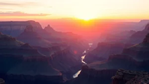 Dramatic sunrise over the Grand Canyon with layered rock formations glowing in golden light, Colorado River visible below, expansive view of canyon depths and distant ridges
